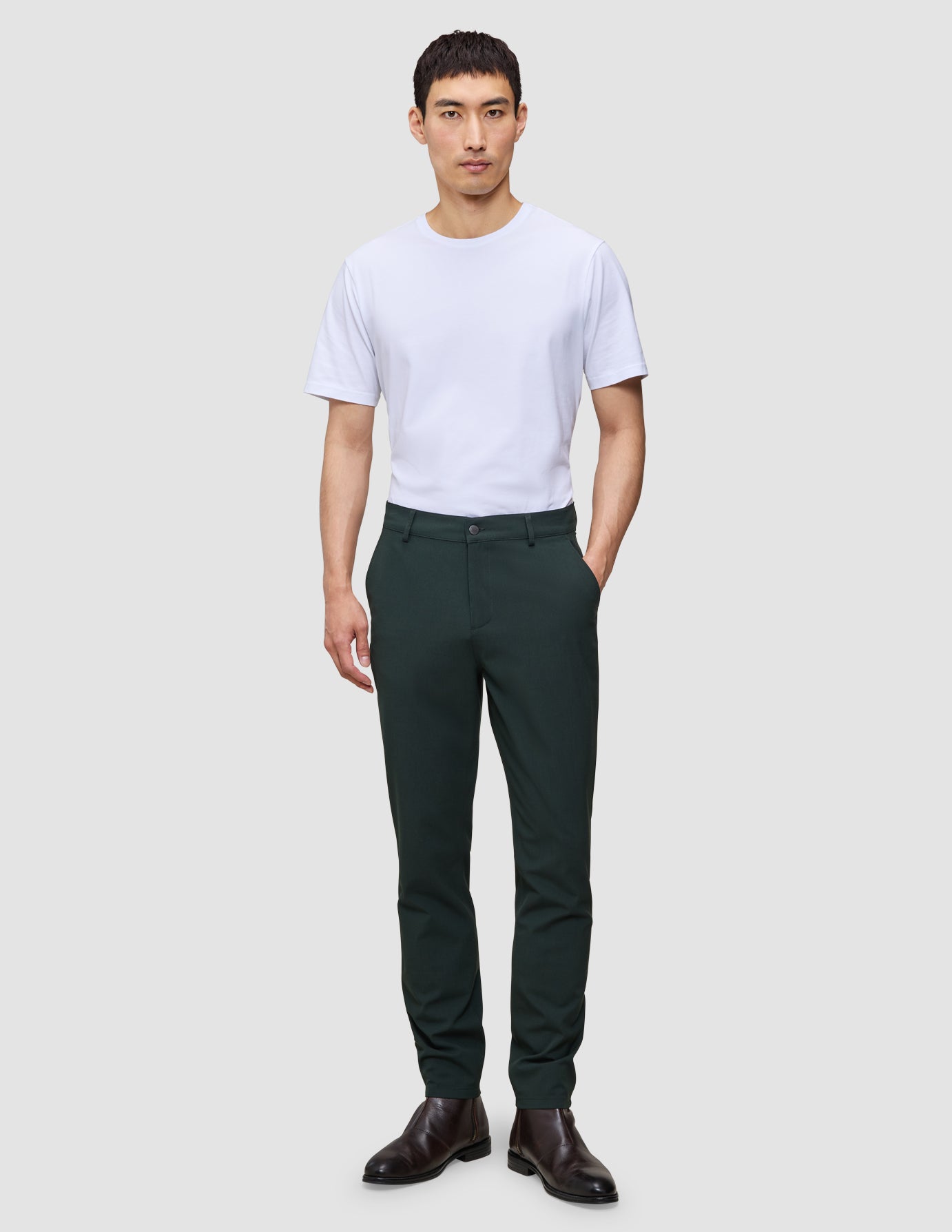 En mand har en hvid T-shirt på, et par mørkegrønne Ease Pants Slim Northern Pine i slim fit samt brune lædersko.